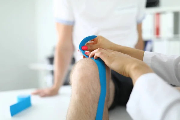 Kniegelenk des Kinesiotapes wird in Arztpraxis am Patienten befestigt. — Stockfoto