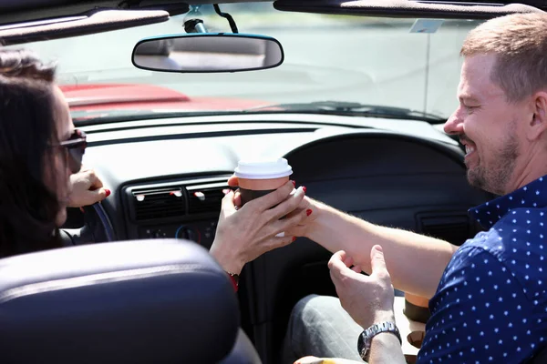 Mann und Frau sitzen lächelnd im Auto und halten ein Glas Kaffee. — Stockfoto