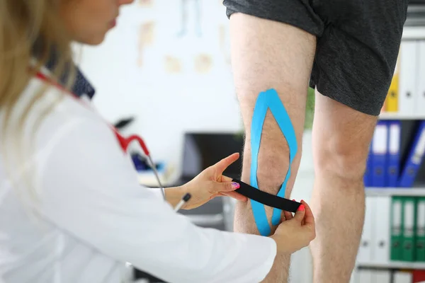 Доктор приклеивает эластичную ленту к ноге пациента — стоковое фото