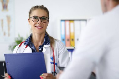 Kadın doktor gülümsüyor ve elinde pano tutuyor..