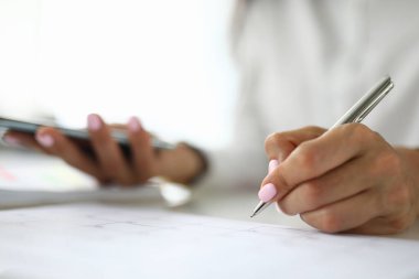 Kadın eli kalem ve telefonu diğer elde tutar.