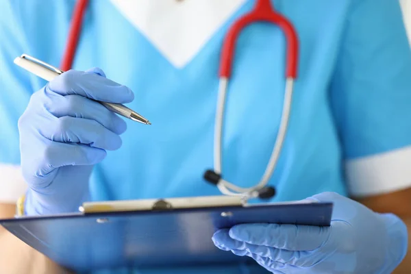 Handschuhdoktor hält Klemmbrett und schreibt hinein. — Stockfoto