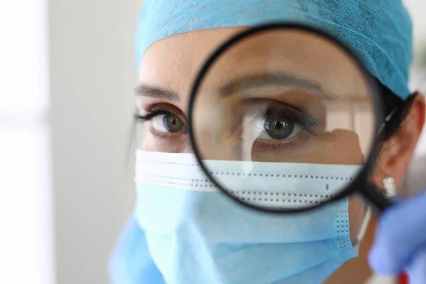 Doctor woman with medical mask looks through magnifying glass