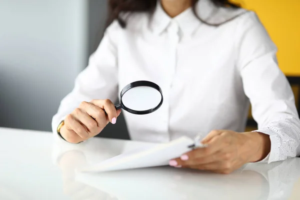 Femme s'assoit à table et tient loupe et documents dans ses mains. — Photo