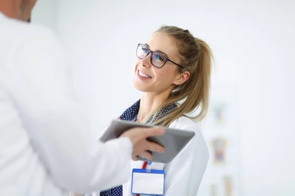 Mujer con bata blanca sonríe y se comunica con un empleado sosteniendo la tableta en sus manos. — Foto de Stock