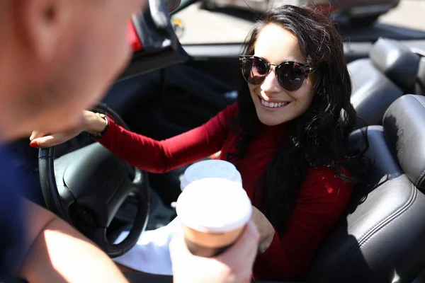 Mujer se sienta en el coche sonriendo sostiene el café en sus manos al lado del hombre. — Foto de Stock