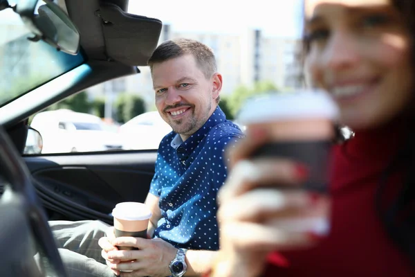 Hombre y mujer están sentados en el coche sonriendo y tomando café — Foto de Stock
