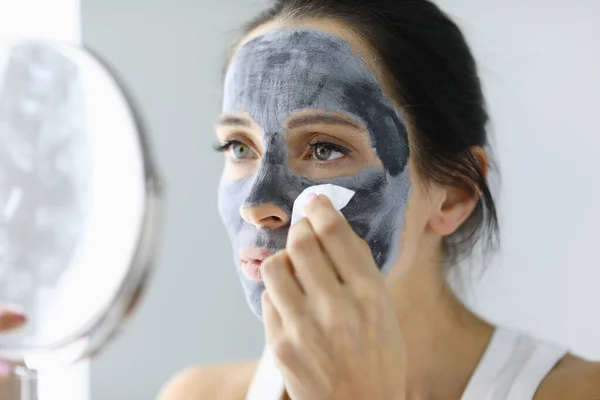 Woman looks in mirror and rinses off cosmetic mask.