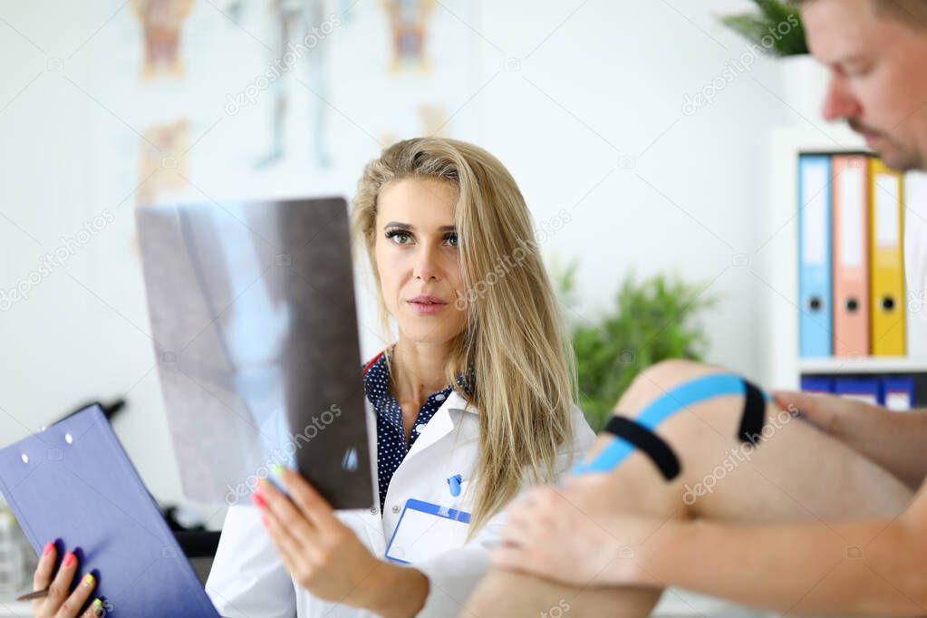 Doctor woman with examines an x-ray of leg next to patient sits.