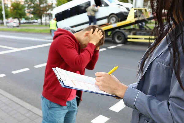 Agent ubezpieczeniowy wypełnia ubezpieczenie po wypadku samochodowym kierowca stoi obok niego i trzyma głowę — Zdjęcie stockowe