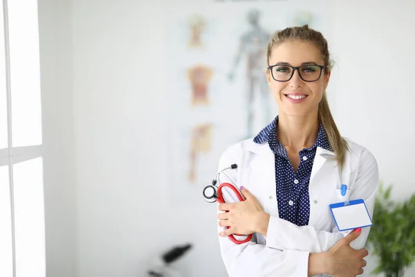 Médica no consultório médico está segurando um estetoscópio e sorrindo — Fotografia de Stock