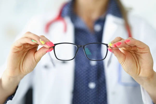 Жінка в білому медичному пальто тримає окуляри в руках . — стокове фото