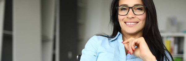 Businesswoman in glasses sits at a table in office and smiles.