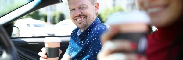 Hombre y mujer están sentados en el coche riendo y bebiendo café . — Foto de Stock