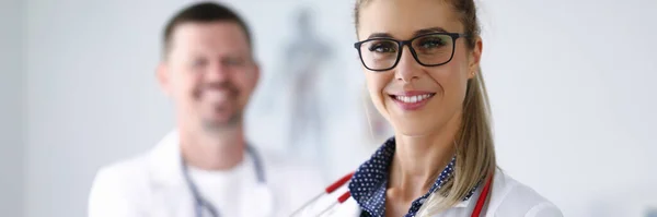 Médica sorrindo e segurando prancheta de trás de sua colega está de pé . — Fotografia de Stock
