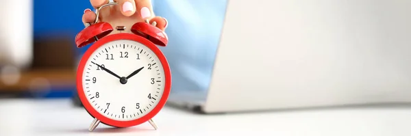 Female hand lies on red alarm clock next to laptop. — Stock Photo, Image