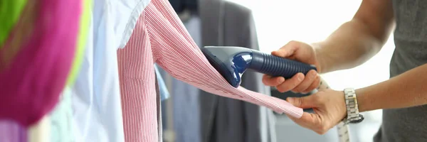 El hombre sostiene el vapor en sus manos y la camisa de planchar en la percha — Foto de Stock