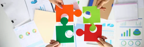 Businessmen hold multicolored puzzles in hand above table with commercial indicators. — Stock Photo, Image