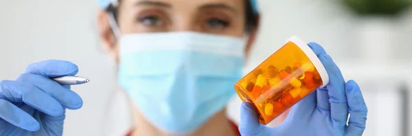 Femme médecin dans le masque tient pot de médicaments et stylo dans sa main — Photo