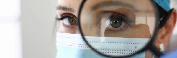 Médico mulher com máscara médica olha através de lupa — Fotografia de Stock