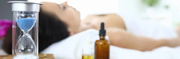 Vrouw ligt in spa salon naast een zandloper en aromatische oliën — Stockfoto