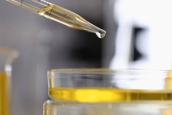 Dávkovač naplněný žlutou chemickou tekutinou lije kapku do skleněné misky detailní — Stock fotografie
