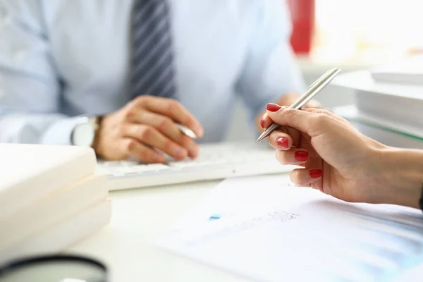 La mano femenina sostiene el bolígrafo sobre los documentos de primer plano delante del hombre en segundo plano en la oficina — Foto de Stock