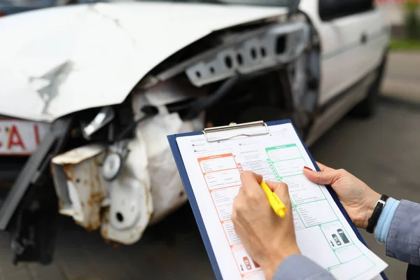 Försäkringsagent håller urklipp och kulspetspenna närbild och kraschade bil i bakgrunden — Stockfoto