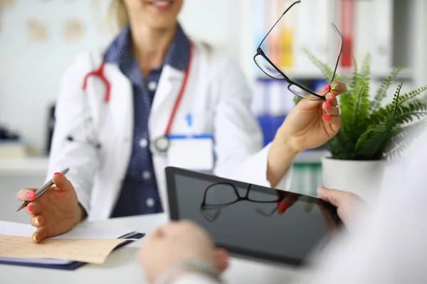 Los médicos con tabletas y gafas en las manos están sentados a la mesa en la reunión en primer plano de la clínica —  Fotos de Stock