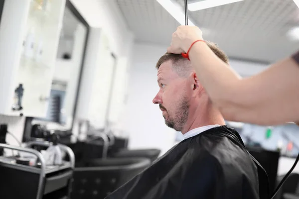 Young man sits in hairdressing chair and makes haircut in beauty salon portrait