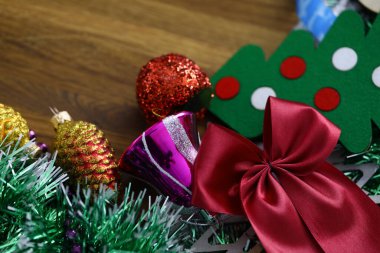 Kırmızı kurdele, Noel oyuncakları, süsler ve diğer süslemeler ahşap masaya yakın duruyor.