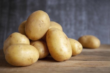 Eski tahta masanın üzerine patates yığını. Koyu arka plan.