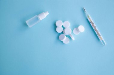 Termometre, haplar ve burun damlaları mavi bir arka plan üzerinde