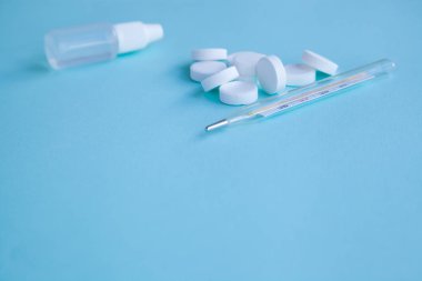 Termometre, haplar ve burun damlaları mavi bir arka plan üzerinde