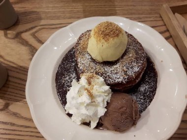 Dondurma Vanilya bir çikolatalı kek üzerine yerleştirilen pudra şekeri serpin, krem şanti ile süsleyin, Dondurma Flavor Çikolata. Güzel beyaz bir çanak üzerinde düzenlenmiş, ahşap bir masa üzerinde