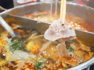 Restoranda sıcak tencerede yemek çubukları ile dilimlenmiş domuz tutun Closeup, Shabu Kore geleneksel veya Sukiyaki Japon geleneksel