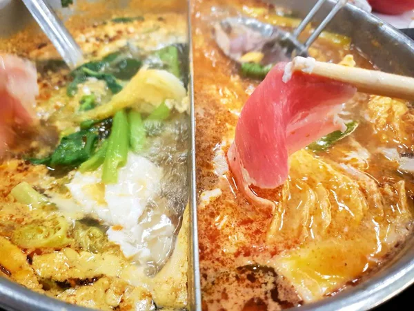 Restoranda sıcak tencerede yemek çubukları ile dilimlenmiş domuz tutun Closeup, Shabu Kore geleneksel veya Sukiyaki Japon geleneksel