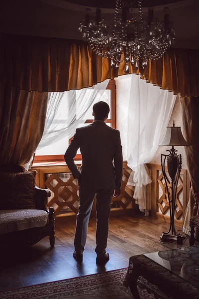 Groom getting ready in the morning in the room. man hands putting on jacket and bow tie, standing at window light in hotel. preparation for wedding day