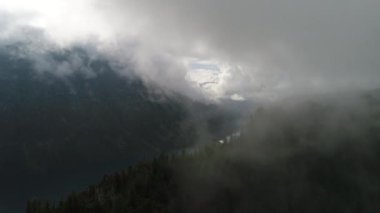  Sedirlerle dolu bir dağın üzerinde bir bulutun içinden göle uçan drone