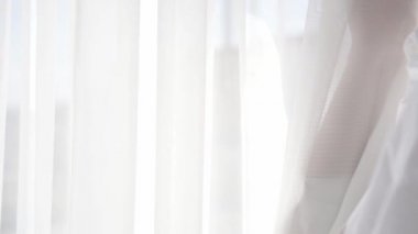 Beyaz gömlekli kız beyaz perdelerin yanında duruyor.
