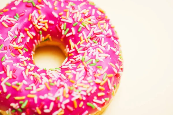 Bright donut in a pink glaze with a multi-colored rainbow sprinkle on a yellow background.