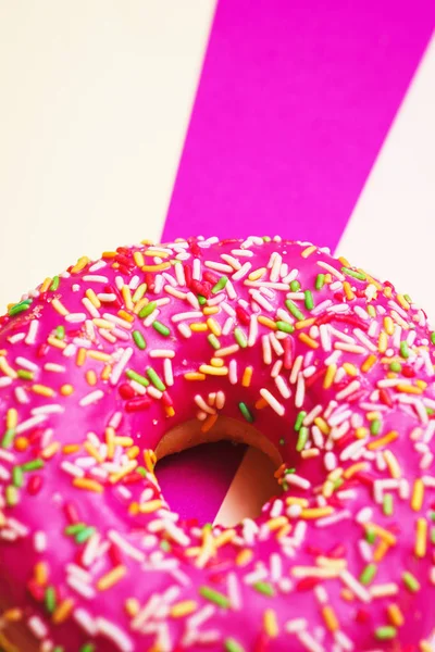 Bright pink sweet donut with pink icing and multi-colored powder on a multicolored background.