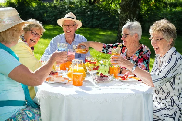 テーブルの周りに座って フルーツケーキを食べて オレンジジュースを飲む幸せな高齢者 — ストック写真