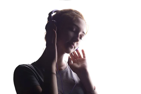 Silhueta de uma menina romântica ouvindo música em fones de ouvido, jovem relaxante em um fundo isolado branco, conceito de hobby e lazer — Fotografia de Stock