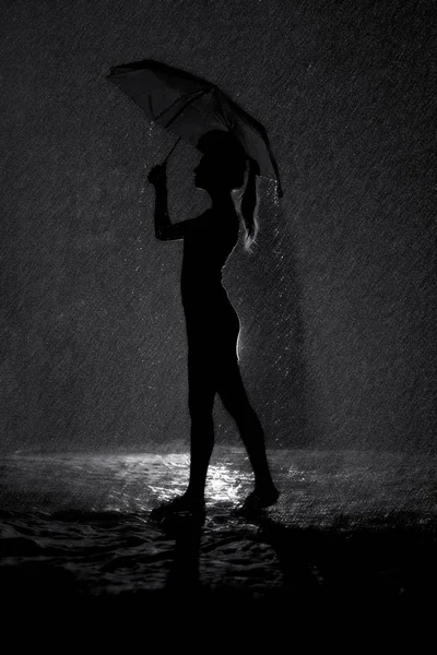 Zwart-wit silhouet van de figuur van een jong meisje met een paraplu in de regen, concept weer en stemming — Stockfoto