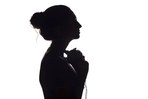 Silhouette di una ragazza con le cuffie intorno al collo, una giovane donna che ascolta musica su uno sfondo bianco isolato, concetto di hobby e relax — Foto Stock