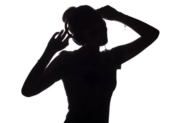 Silhouette of a active girl listening to music in headphones, figure of young woman dancing with hands up on a white isolated background — Stock Photo, Image