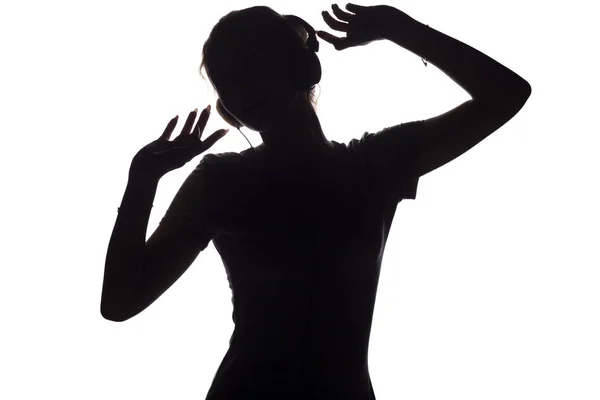 Silhouette di una ragazza felice che ascolta musica in cuffia, figura di giovane donna con le mani alzate che si rilassa su uno sfondo bianco isolato e balla sulla musica — Foto Stock