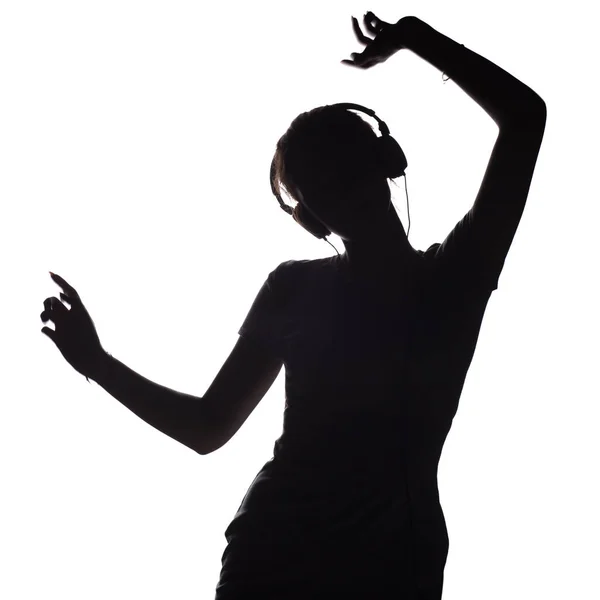 Silhueta de uma garota ativa ouvindo música em fones de ouvido, figura de jovem dançando com as mãos para cima em um fundo isolado branco — Fotografia de Stock