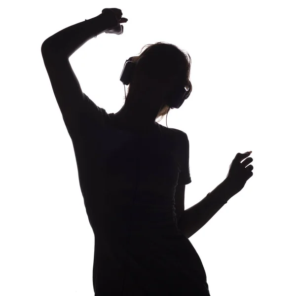 Silueta de una chica activa escuchando música en auriculares, figura de una joven bailando con las manos en alto sobre un fondo blanco aislado —  Fotos de Stock